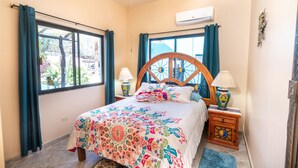 A bedroom with a bed, two bedside tables, a window, and an air conditioning unit. - Heart of Los Barriles Ocean View and Pool (Los Barriles)