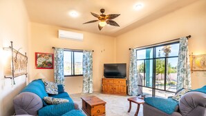 A spacious living room with a large sofa set, a wooden cabinet with a flat-screen TV, and a ceiling fan. - Heart of Los Barriles Ocean View and Pool (Los Barriles)