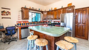 A kitchen with wooden cabinets, a large island with stools, a refrigerator, and a colorful backsplash. - Heart of Los Barriles Ocean View and Pool (Los Barriles)