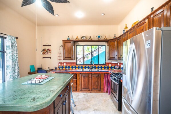 Una cocina con armarios de madera, un refrigerador de acero inoxidable, un salpicadero colorido y un ventanal con vistas.
