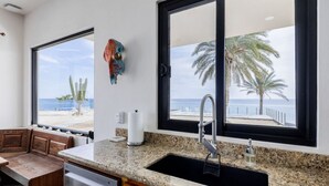 A kitchen with granite countertops, a built-in dishwasher, and a large window overlooking a beach.