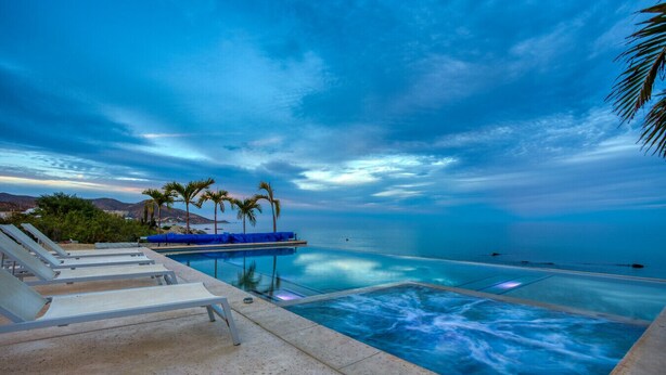 An infinity pool with a view of the ocean, lounge chairs, and palm trees.