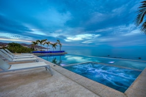 Ein Infinity-Pool mit Blick auf den Ozean, Liegestühle und Palmen.