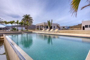 Une piscine entourée de chaises longues, de palmiers et, au loin, de bâtiments modernes.