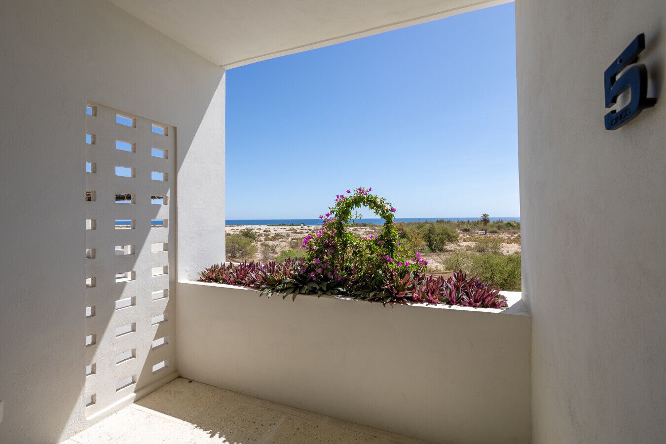 A balcony with a view of the sea, a white wall, and a blue sign with the number 5.
