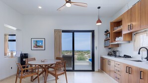 A modern kitchen with wooden cabinets, a dining area with a table and chairs, and a view of the outdoors through a sliding glass door. - Pool Condo, just a few steps from the beach -north (Los Barriles)