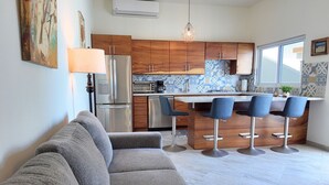 Una cocina moderna con armarios de madera, una isla central con taburetes altos y un amplio ventanal que proporciona luz natural.