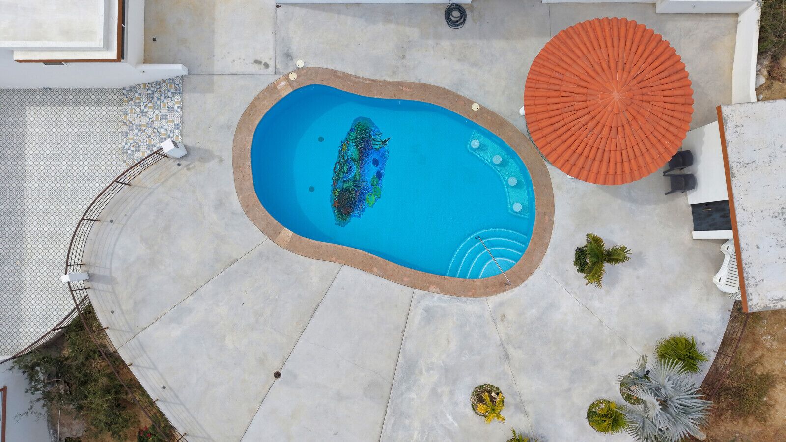 Luchtbeeld van een zwembad met betegeld terras, een zonnescherm en een kleine tuin.