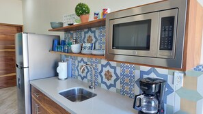 Una cocina moderna con refrigerador de acero inoxidable, microondas, cafetera y pileta.