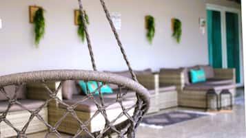 Une chaise en osier avec un filet en corde, un canapé agrémenté d’un coussin turquoise et des plantes vertes sur le mur.