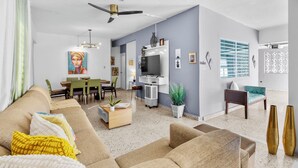 A modern living room with a sofa, coffee table, and a dining area with chairs and a TV. - Water tank 5 Min Airport & Beach Jacuzzi, BBQ-Kids Pool,Ping Pong -Solar Panels (Carolina)