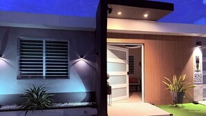 A modern house with a well-lit entrance, a visible door, and a small outdoor seating area. - Water tank 5 Min Airport & Beach Jacuzzi, BBQ-Kids Pool,Ping Pong -Solar Panels (Carolina)
