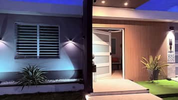A modern house with a well-lit entrance, a visible door, and a small outdoor seating area.