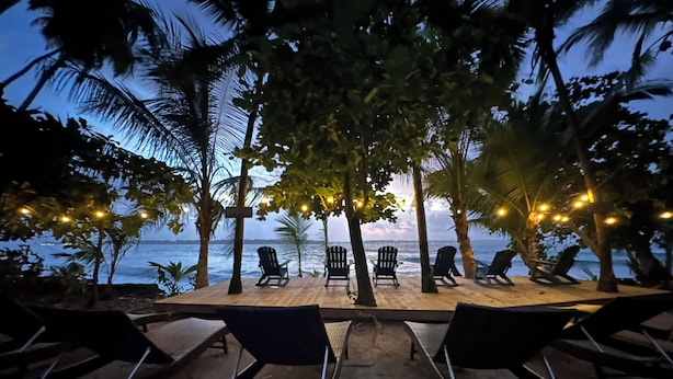 Een strandlounge met stoelen en tafels, palmbomen en uitzicht op de oceaan.