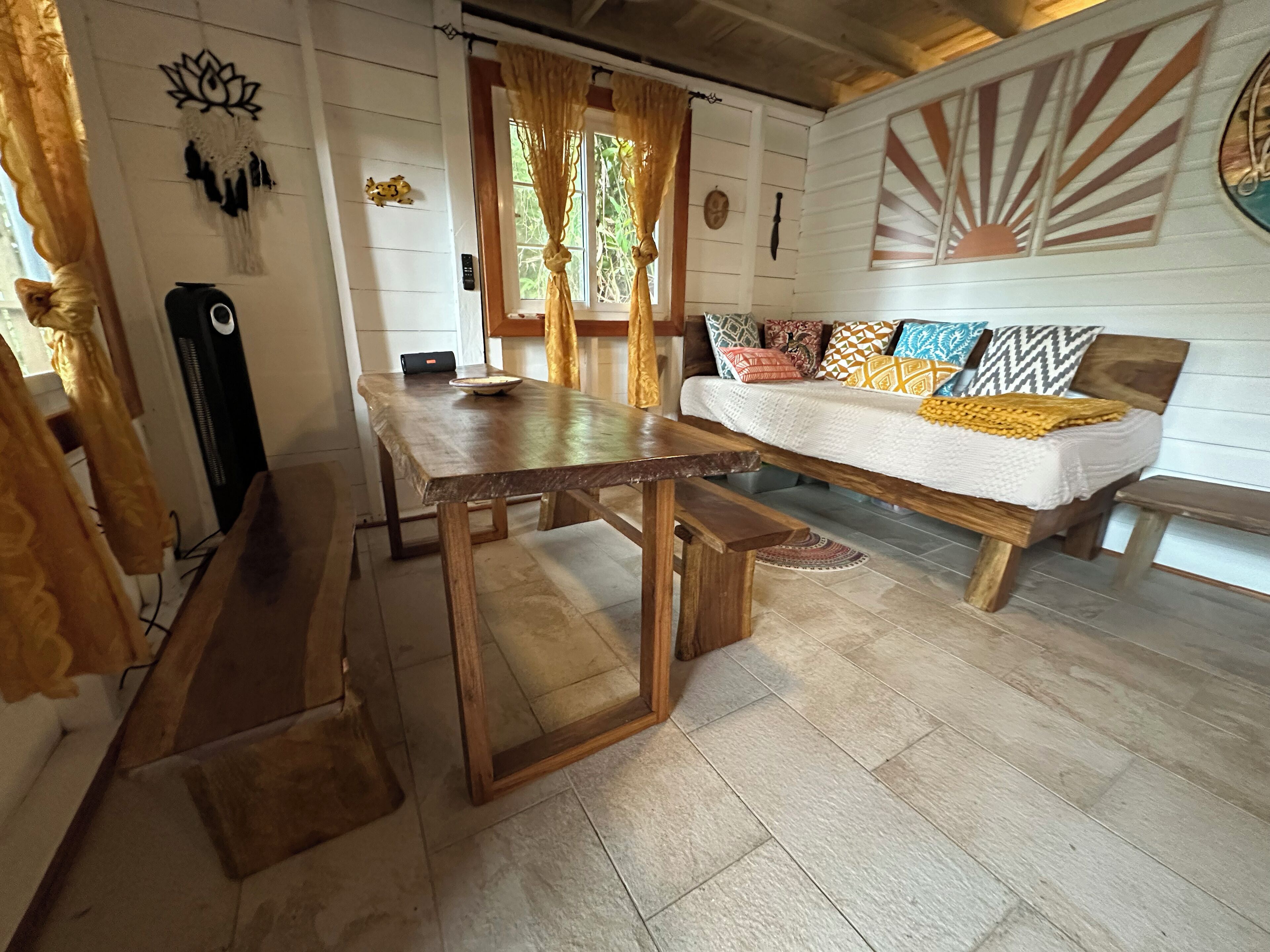 A cozy living room with a wooden table and bench, a sofa with patterned cushions, and a wall with decorative elements.