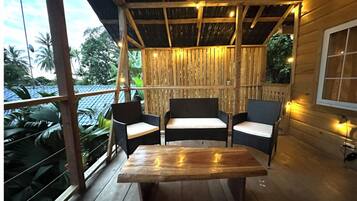 Una terraza de madera con una mesa, sillas, ventanas amplias y una pared de bambú.