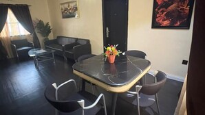 A room with a black marble table, four chairs, a sofa, a door, and a painting on the wall. - Cozy 1-BEDROOM WITH AC, WiFi, FULL kitchen, free parking, restaurant delivery (Satellite Town)