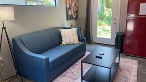 A living room with a blue sofa, a coffee table, a lamp, a painting, and a red refrigerator.