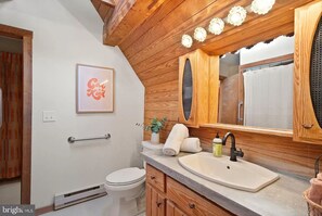 Ein Badezimmer mit Holzboden, einem Waschbecken mit Spiegel, einer Toilette und einem Handtuchhalter.