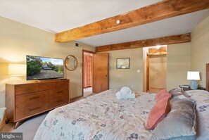Ein Schlafzimmer mit einem Bett, einem Fernseher auf einer Holzkommode, einem Spiegel und einem Bild an der Wand.