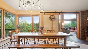 Un comedor espacioso con una mesa y sillas de madera, ventanas amplias que ofrecen vistas a la vegetación y una lámpara moderna.