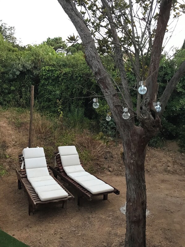 Two wooden lounge chairs with white cushions, positioned under a tree with hanging glass globes. - Paradise, 50 m from the beach on the Isolella peninsula. (Pietrosella)