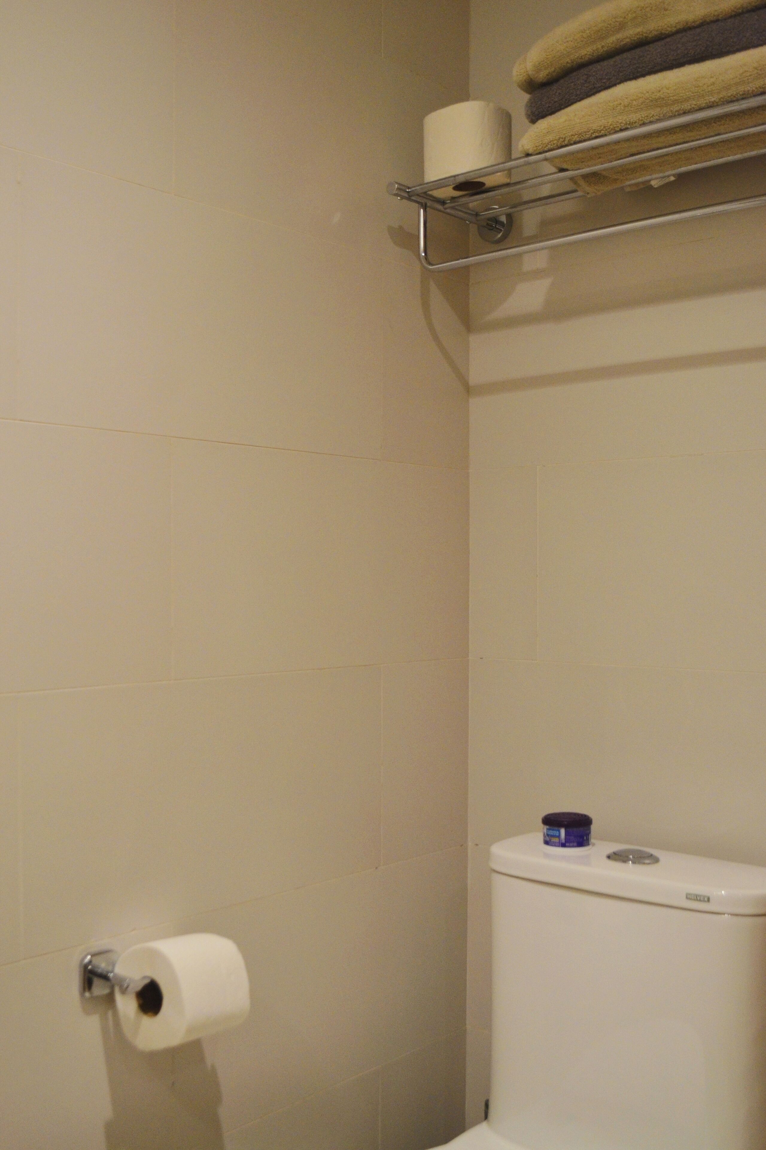 Een badkamer met een toilet, toiletpapier en een plank met handdoeken.