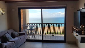 Sala de estar con sofá, televisión montada en la pared y balcón con vista al mar.