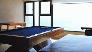 Una mesa de billar con vista al mar a través de amplios ventanales.