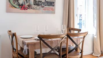 Un coin repas avec une table en bois dressée pour quatre personnes, entourée de chaises en bois à ossature métallique. Une affiche ancienne est accrochée au mur, au-dessus de la table.