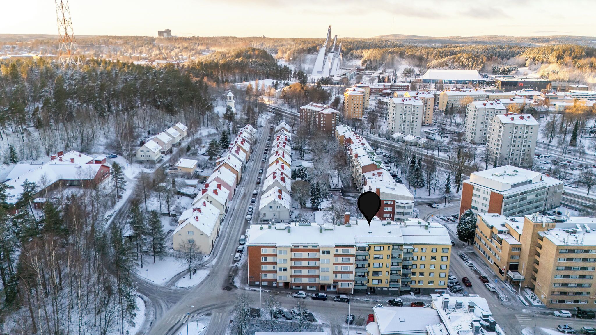 Vista aérea de una zona residencial con varios edificios de apartamentos, carreteras y una gran instalación industrial al fondo.