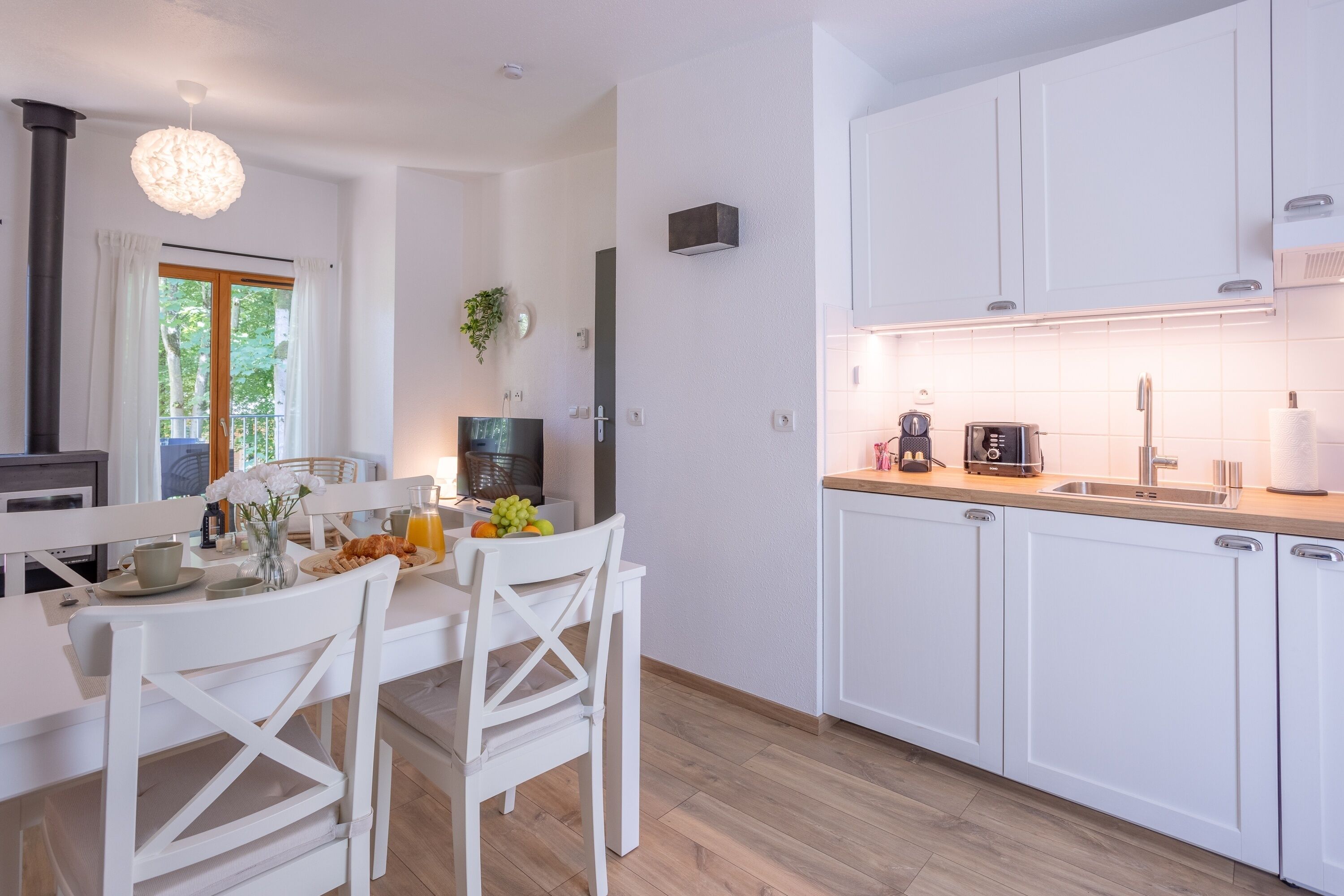 A modern kitchen with white cabinets, a dining area with a table and chairs, and a large window with curtains.