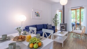 Una sala de estar moderna con un sofá azul, sillas blancas, una mesa de comedor con desayuno y una chimenea.