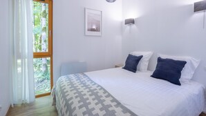 Un dormitorio con cama, ventana con cortinas, lámpara de pared e imagen enmarcada.