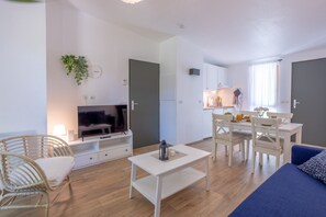 A modern living room with a TV, white furniture, a dining area, and a kitchen.