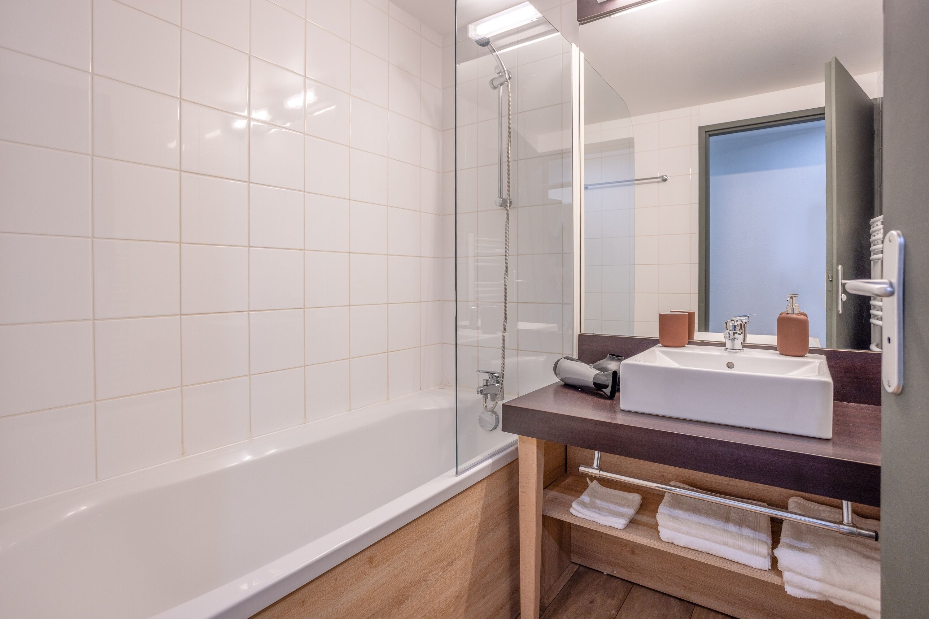 Ein modernes Badezimmer mit einer Duschkabine, einem weißen Waschbecken und einem Holz-Waschtisch.