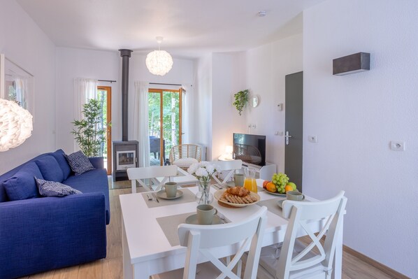 A modern living room with a sofa, dining table, chairs, a TV, and a fireplace.
