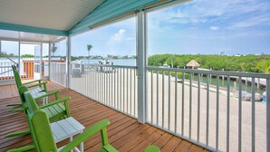 A covered deck with wooden flooring and green chairs, overlooking a body of water with boats and a thatched-roof structure. - Charming 3-bedroom 2-bathroom house with Boat Ramp and Dockage in Marathon (Marathon)