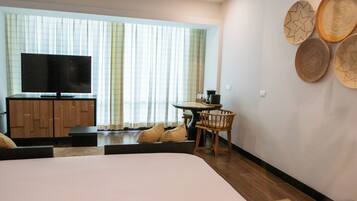 Quarto de hotel com cama, televisão, pequena mesa com cadeiras e pratos decorativos trançados na parede.