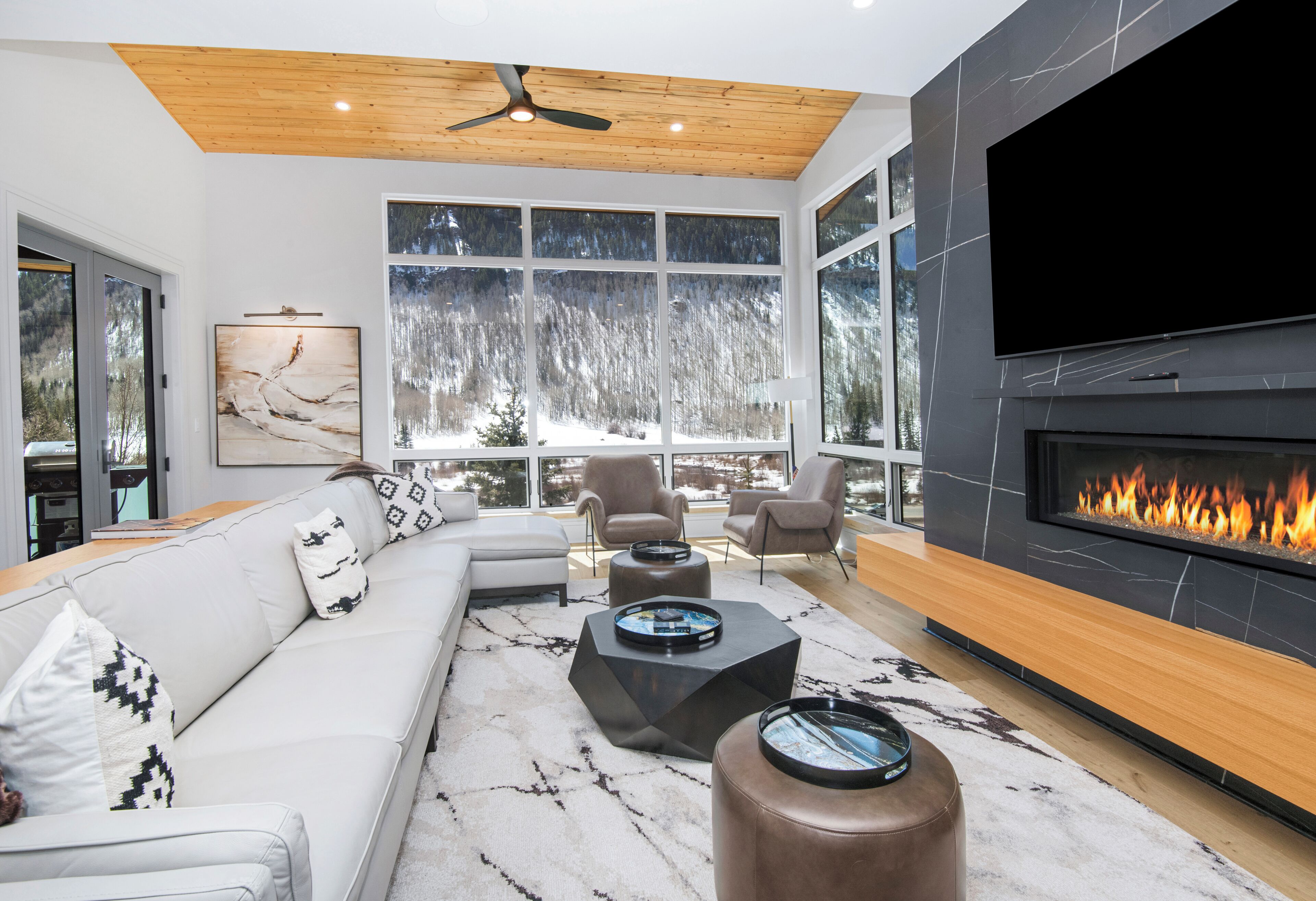 A modern living room with a large TV, fireplace, and large windows with a snowy view.