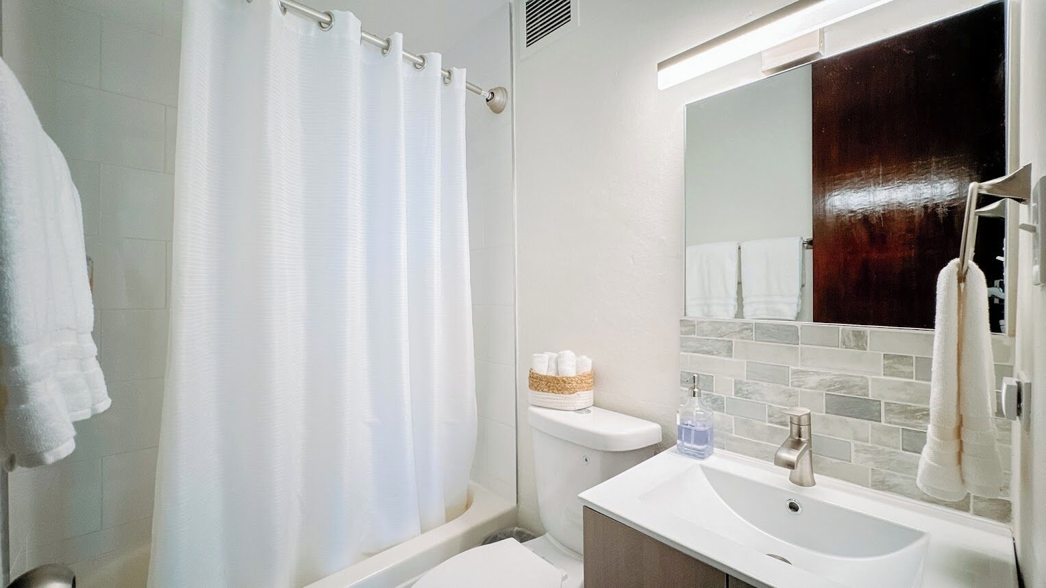 Un baño con cortina de ducha, inodoro, lavamanos con espejo y barra para toallas.
