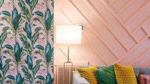 Ein gemütliches Wohnzimmer mit strukturiertem Wandpapier, einer modernen Lampe und einem grauen Sofa mit bunten Kissen.
