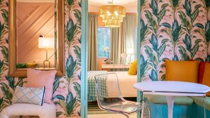 Ein Hotelzimmer mit einem Bett, einem Sessel, einem Tisch, einem Spiegel und einer Chandelier.