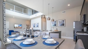 Un comedor moderno con una mesa larga dispuesta para seis, una cocina al fondo y un balcón con barandilla.