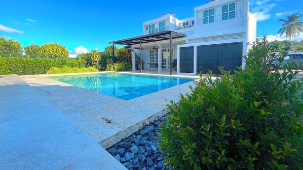 A modern house with a swimming pool, a covered patio, and lush greenery. - Charming 4-bedroom Estate with In-ground pool WiFi in San Juan (Guaynabo)