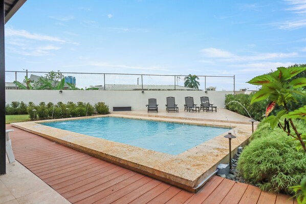 A rectangular swimming pool with a wooden deck, surrounded by a low wall and a fence. - Charming 4-bedroom Estate with In-ground pool WiFi in San Juan (Guaynabo)