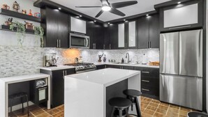 A modern kitchen with dark cabinetry, a central island with stools, a stainless steel refrigerator, and a ceiling fan. - Charming 4-bedroom Estate with In-ground pool WiFi in San Juan (Guaynabo)