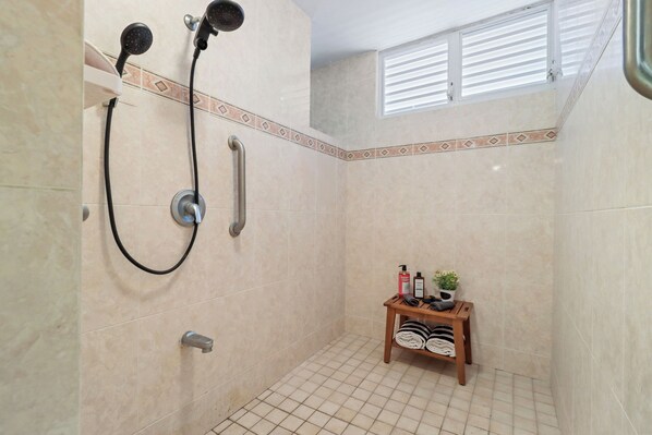 A small, tiled bathroom with a shower, a towel rack, and a shelf with toiletries.