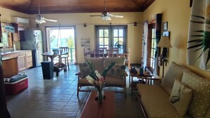 Amplia sala de estar con techo alto, vigas de madera, zona de comedor y cocina equipada con refrigerador.
