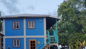 Ein zweistöckiges Haus mit blauer Fassade, einer Holztür und einer Treppe, die zu einer überdachten Veranda führt.